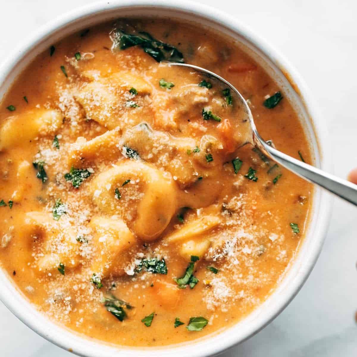 Tortellini Soup with Italian Sausage and Kale in a bowl with a spoon dipping in.