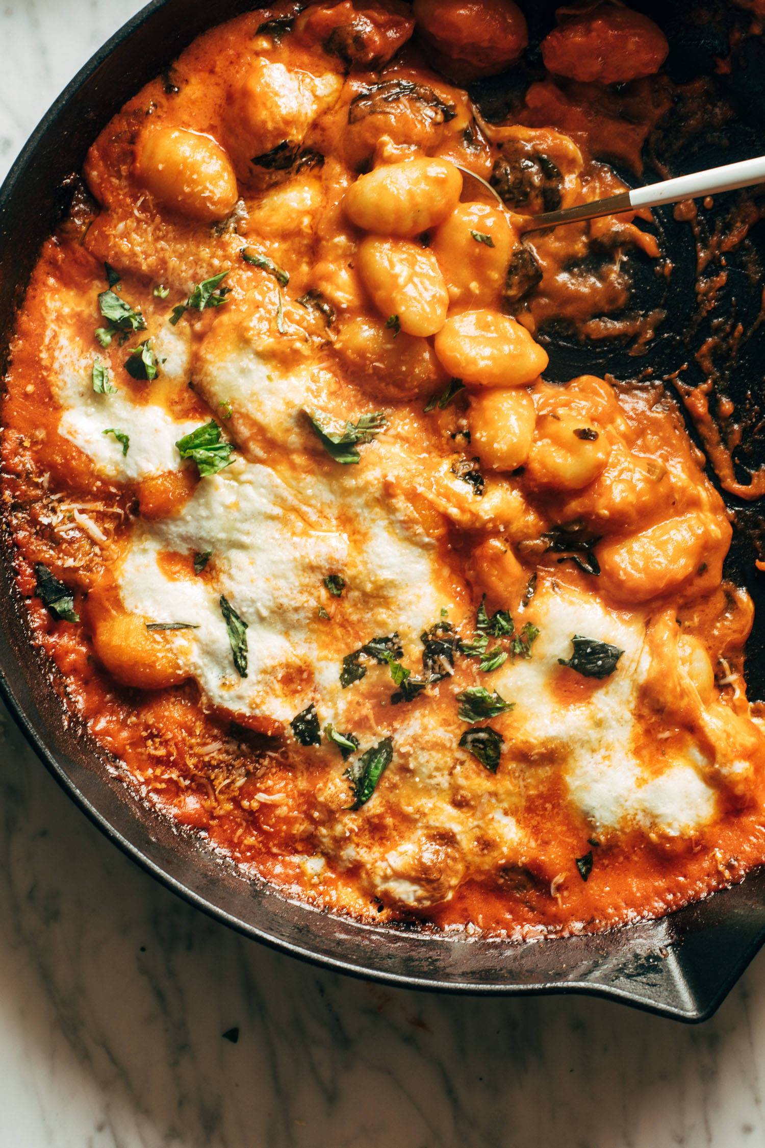 Three cheese baked gnocchi with fresh basil torn on top. The gnocchi is in a cast iron skillet. 