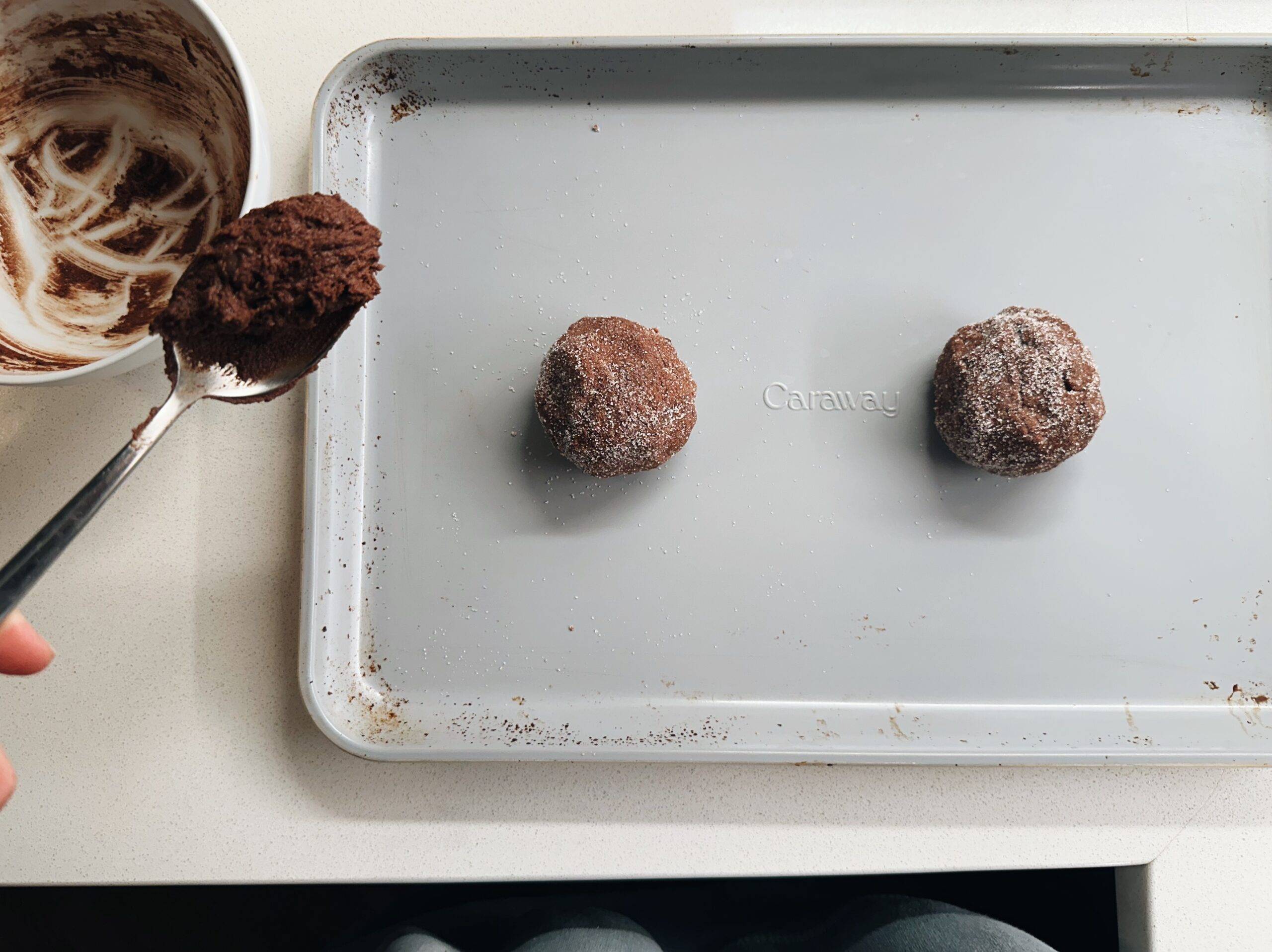 Two cookie dough balls on a sheet pan.