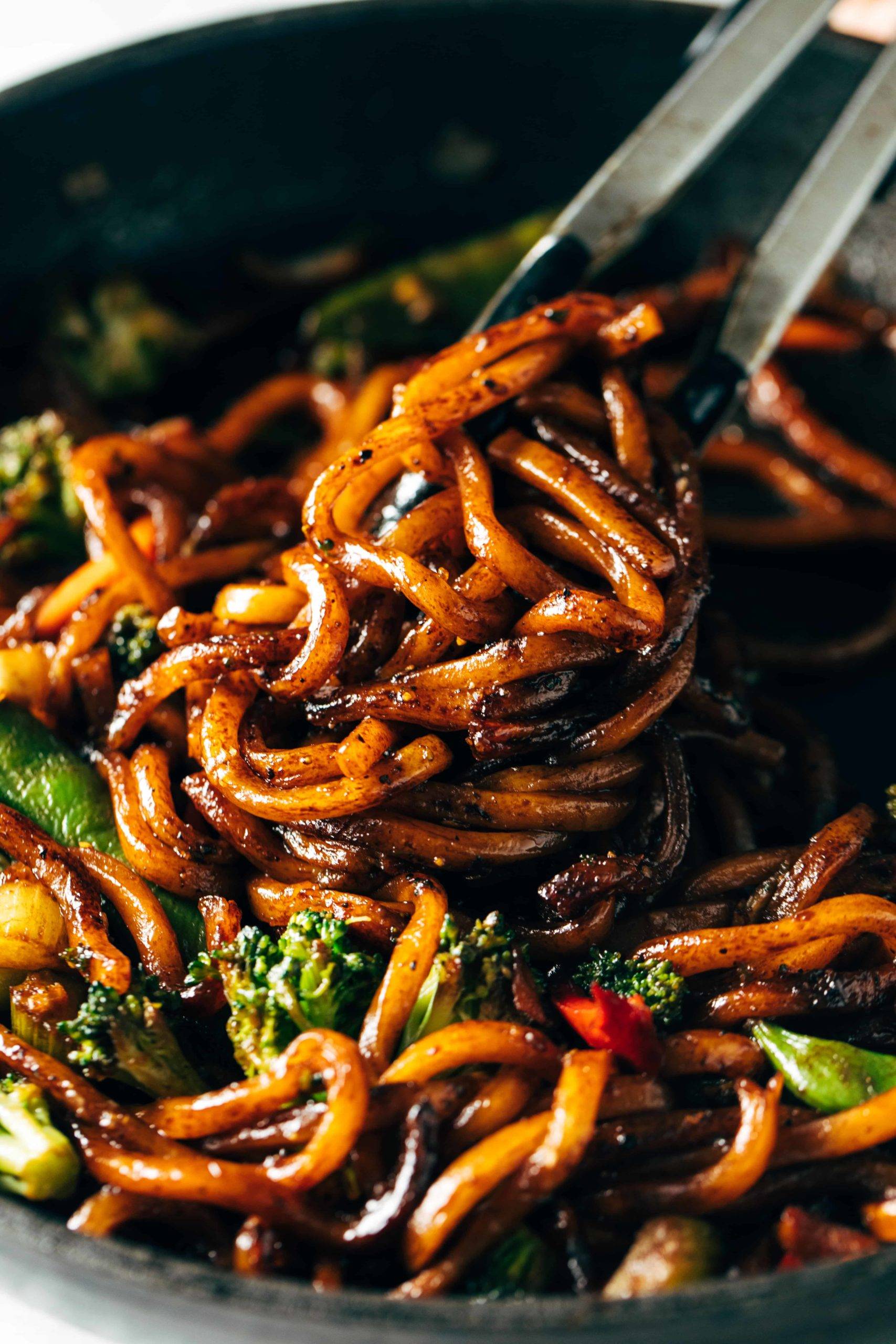 Udon Noodles mixed with fried vegetables and some black pepper in a cooking pan.
