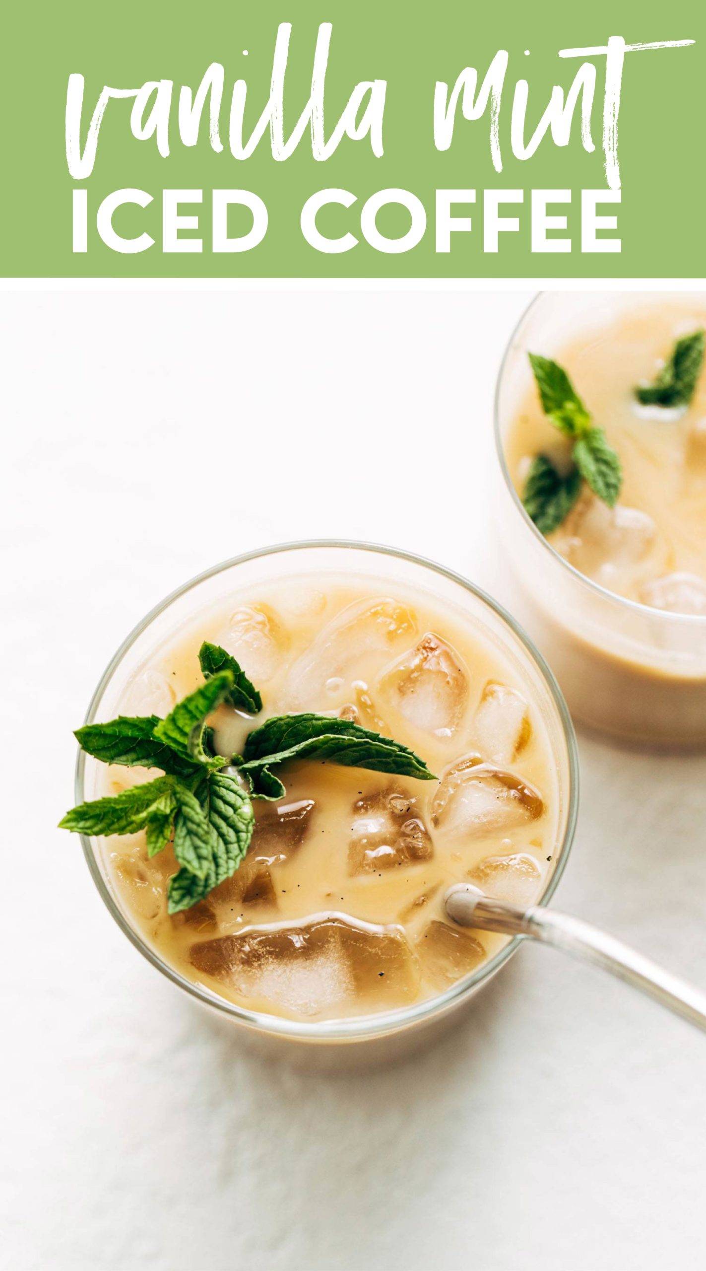 Clear glass with ice cubes, creamy vanilla coffee, and a fresh bundle of mint floating atop next to a silver spoon.