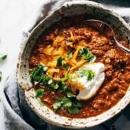 Chunky chili with cilantro, sour cream, and cheddar cheese in a rustic bowl.