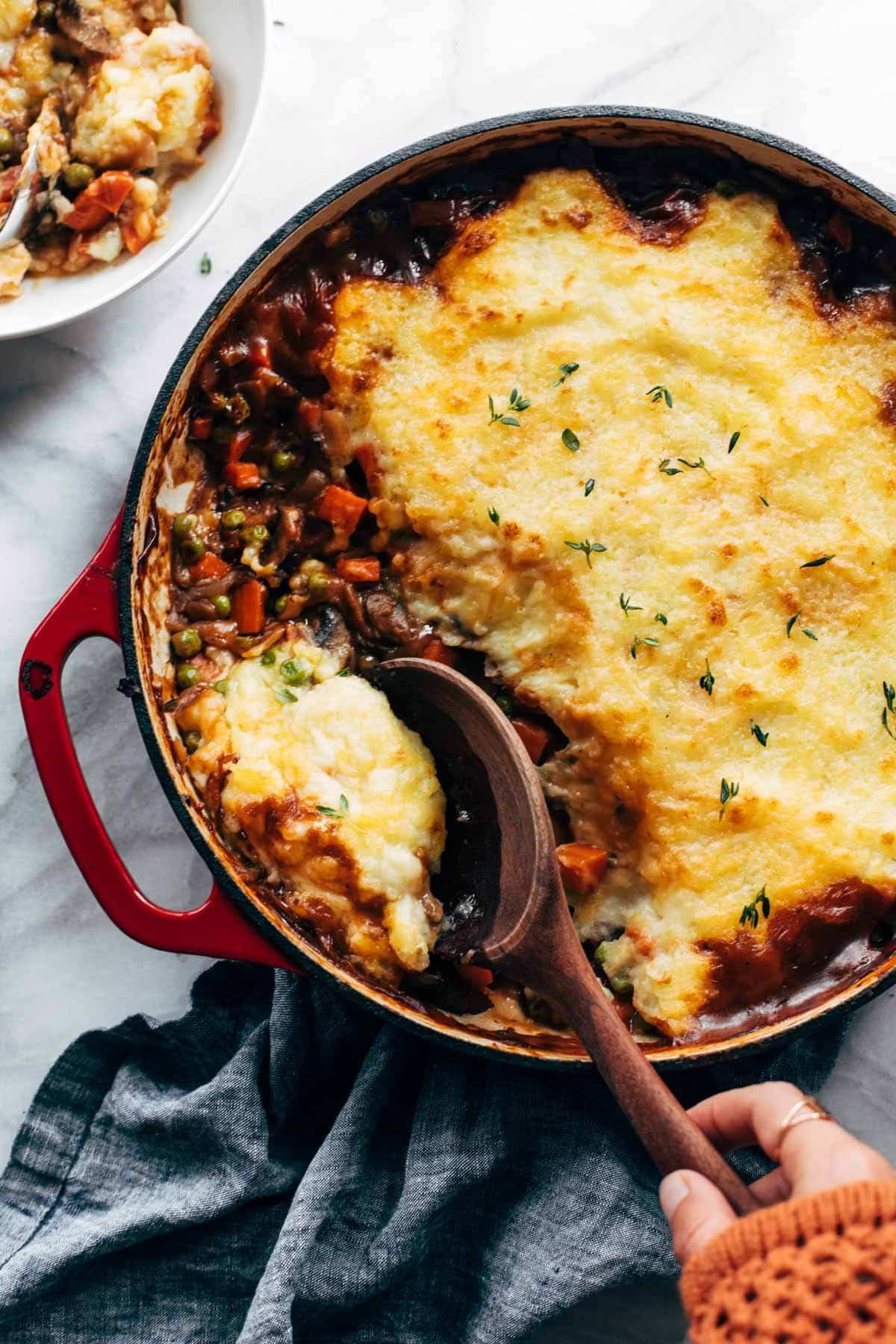 Vegetarian Shepherd's Pie in a red casserole dish being scooped with a wooden spoon