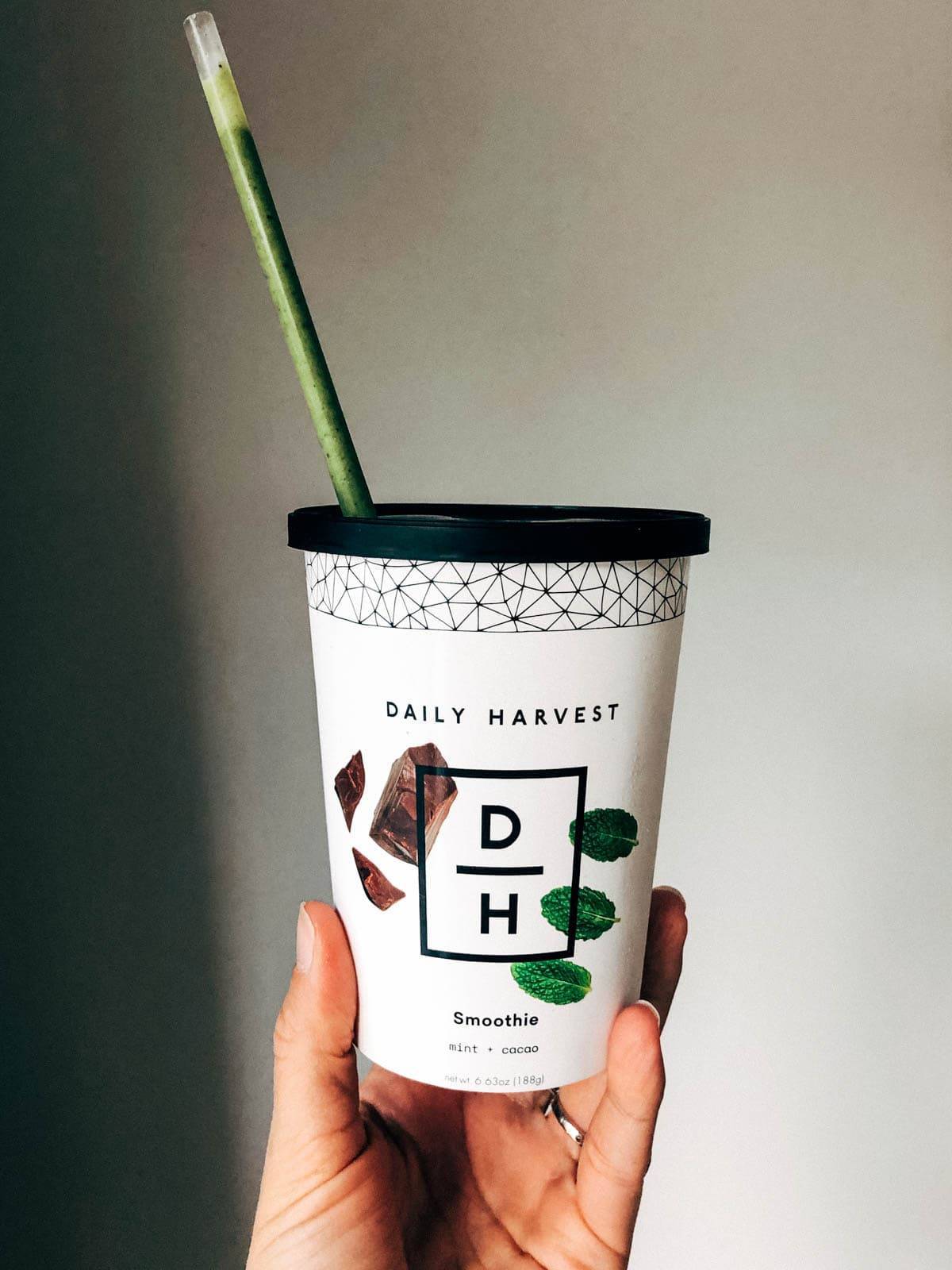 A hand holding a large cup of smoothie named Daily Harvest.