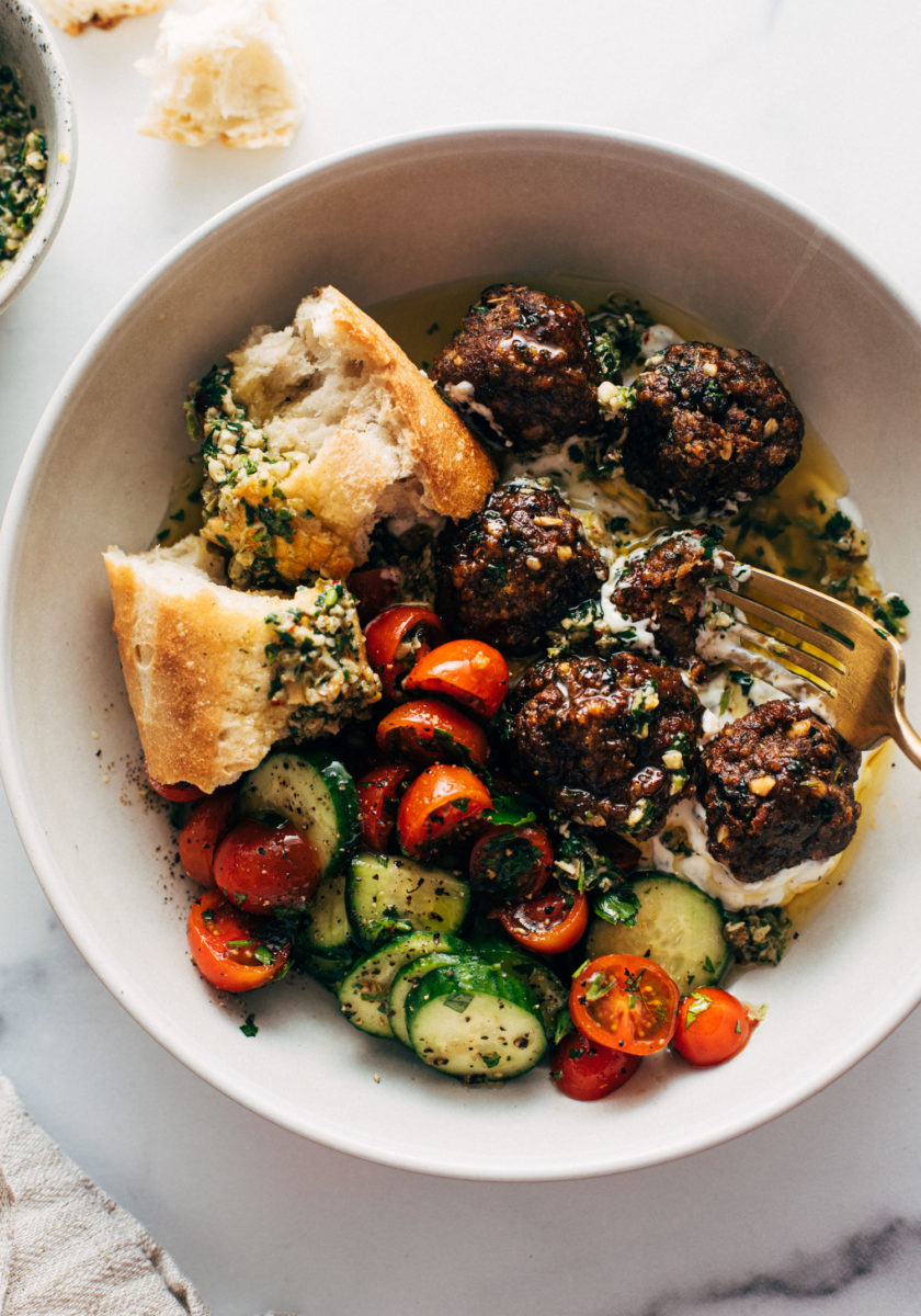 Meatballs in a bowl with a tomato salad, fork, and bread