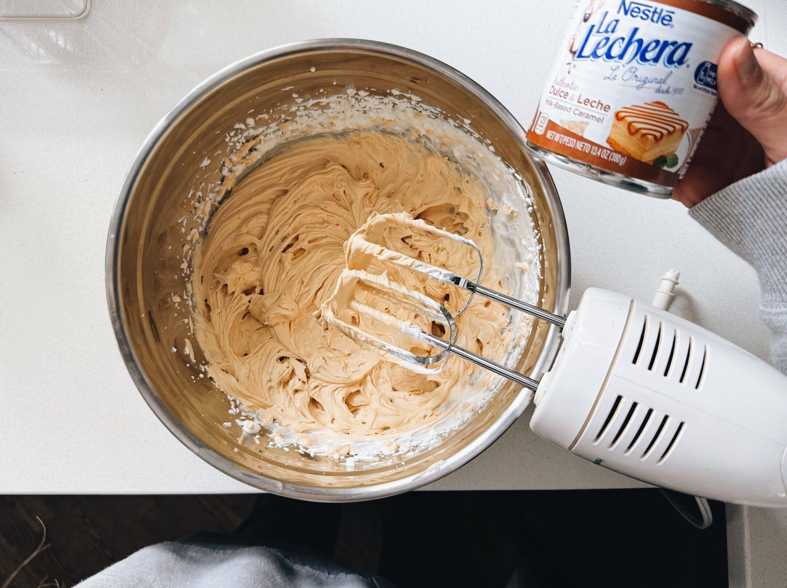 Mixing heavy whipping cream and dulce de leche with an electric hand mixer.