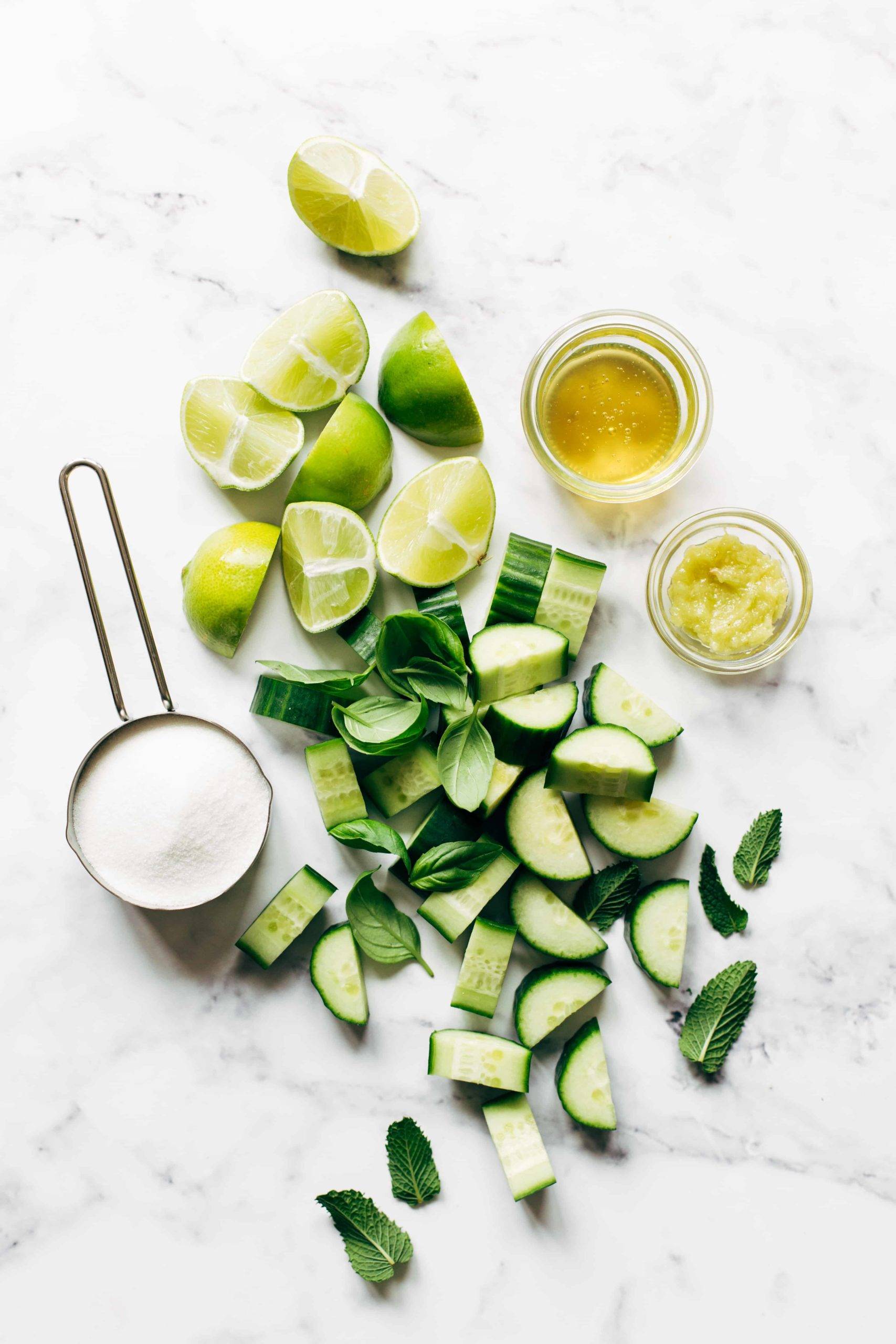 The ingredients for cucumber water include mint, chunks of cucumber, lime wedges, some sugar, some ginger, and some honey.