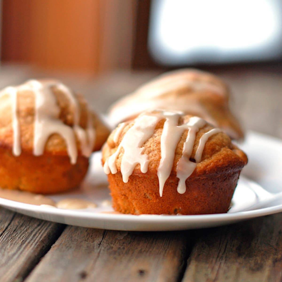 Apple cinnamon muffins topped with a warm vanilla glaze on a white plate.