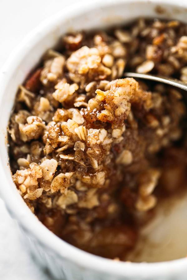 Close up Apple Crisp in a white dish with a spoon.