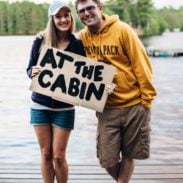 Lindsay and Bjork on the dock holding a sign that says "At the cabin"