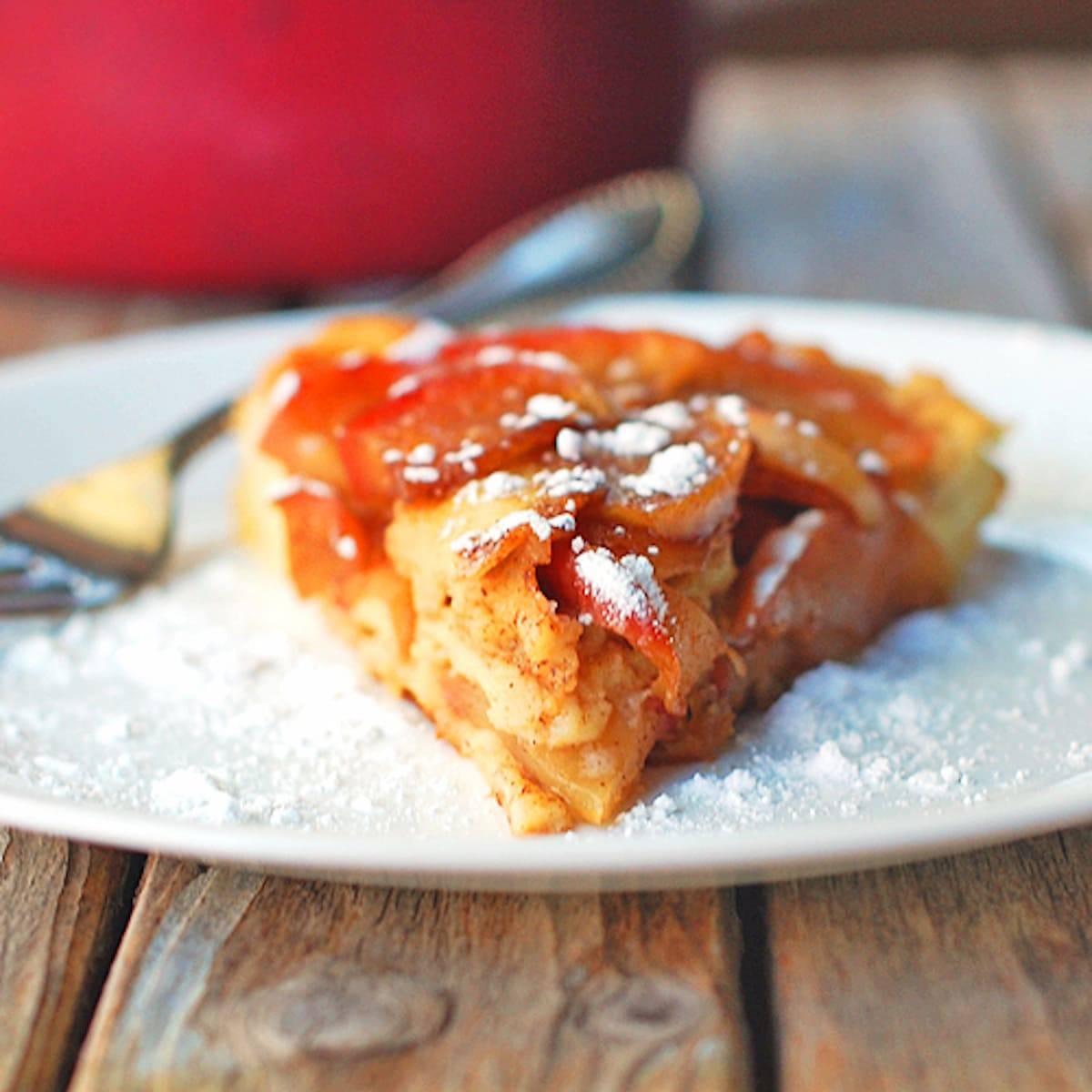 Baked apple pancake is baked in a cast iron skillet and topped with a homemade apple cider syrup on a plate.