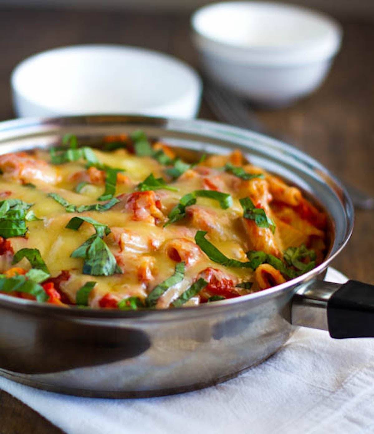 Baked caprese rigatoni with tomatoes, basil, and Mozzarella in a pan.