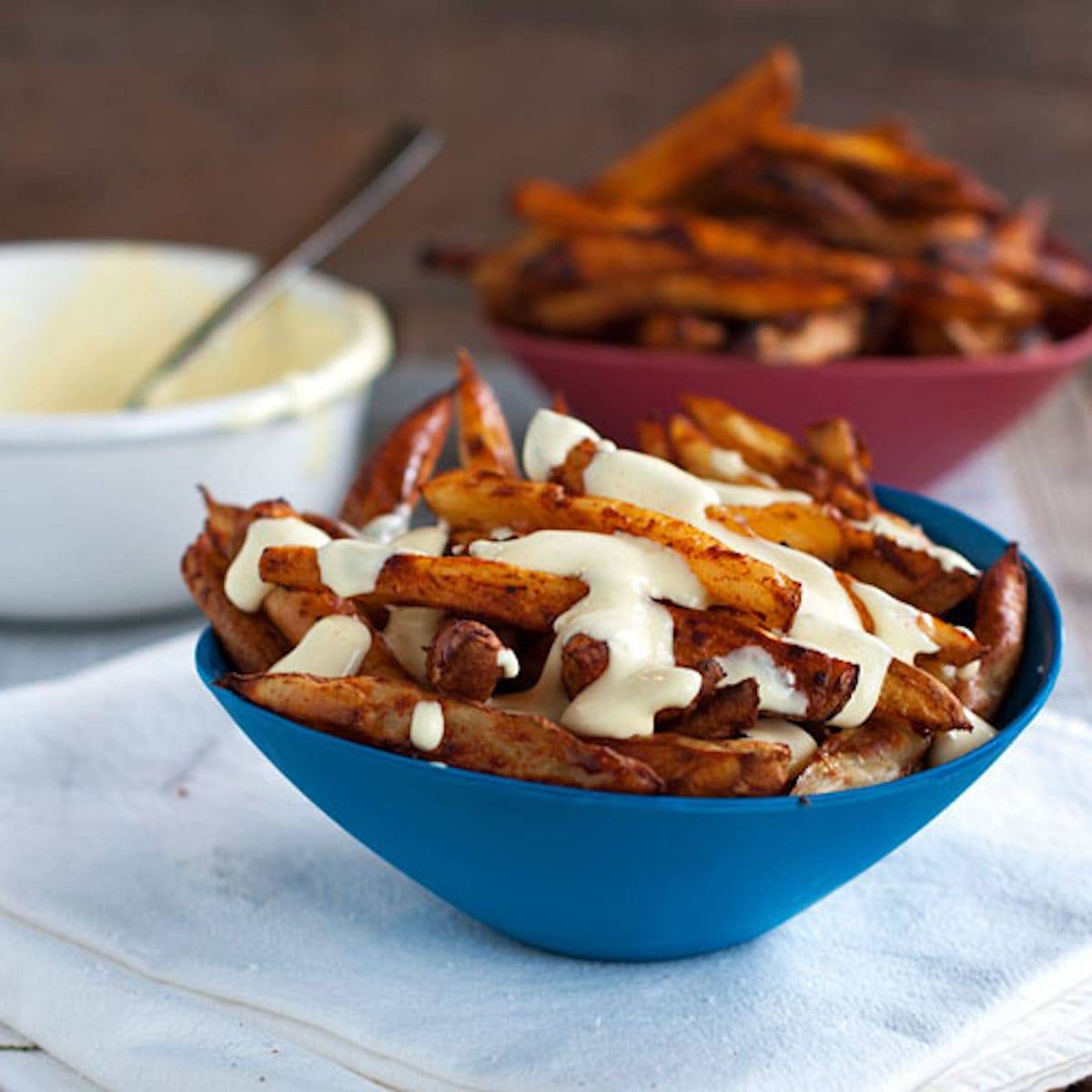 Baked spicy fries topped with a lighter garlic cheese sauce in a blue bowl.