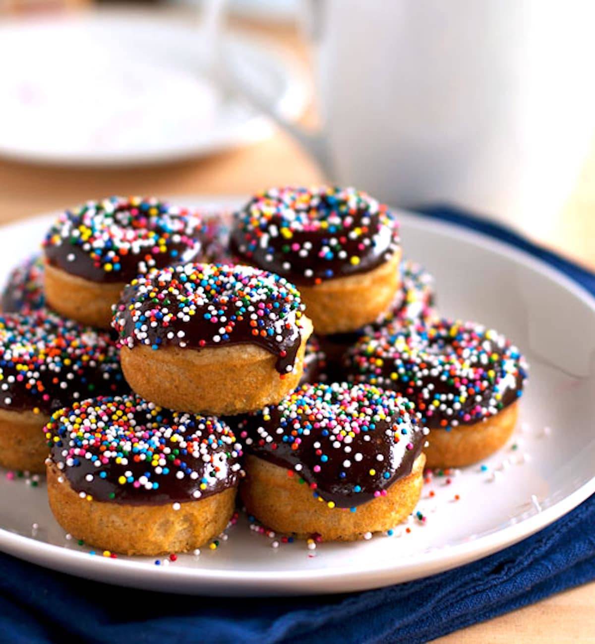 Chocolate glazed baked mini donuts with sprinkles on a plate.