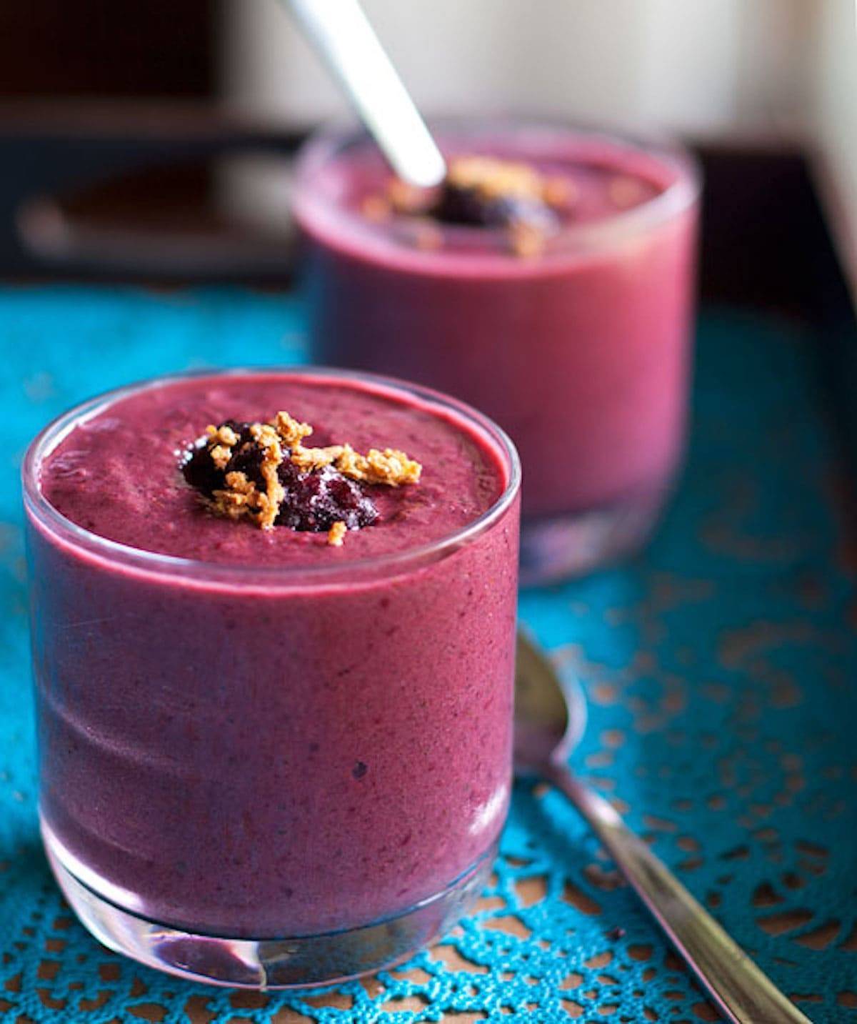Berry green smoothies in glasses on a blue surface.