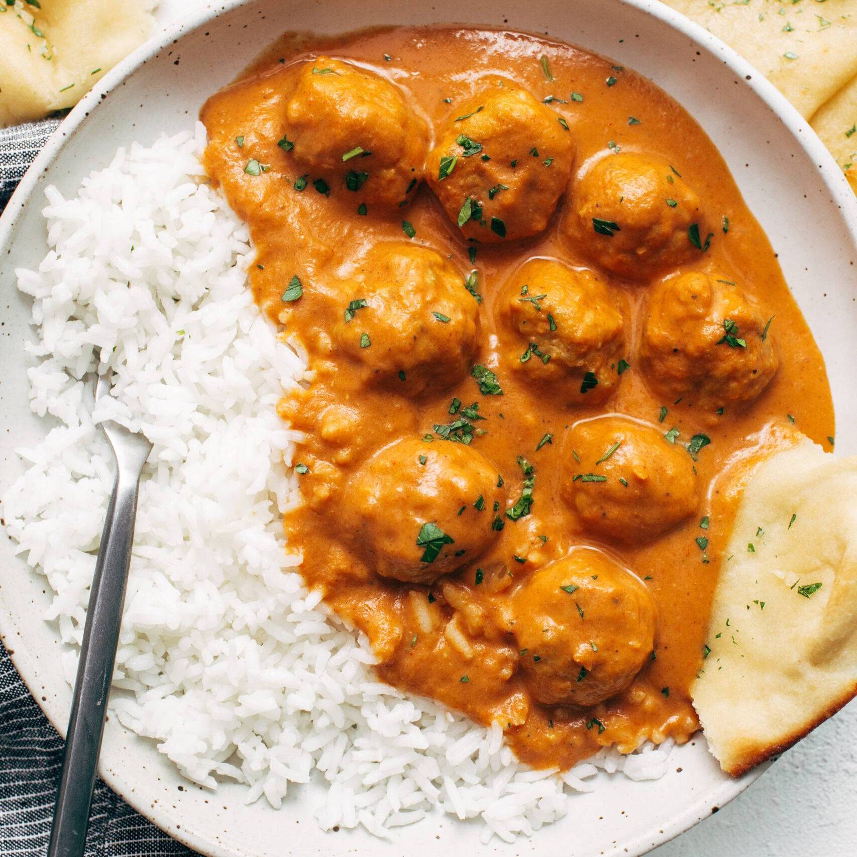 Butter chicken meatballs in a bowl with rice and naan.