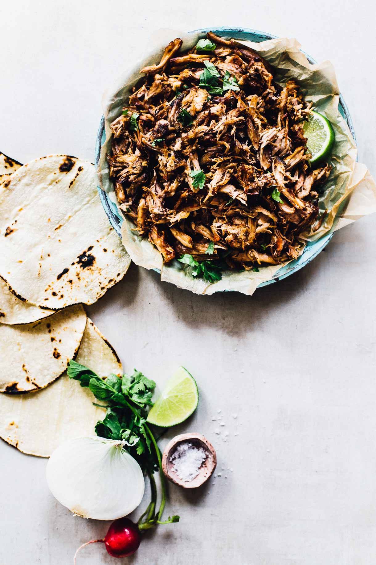 Crockpot carnitas in a bowl with tortillas.