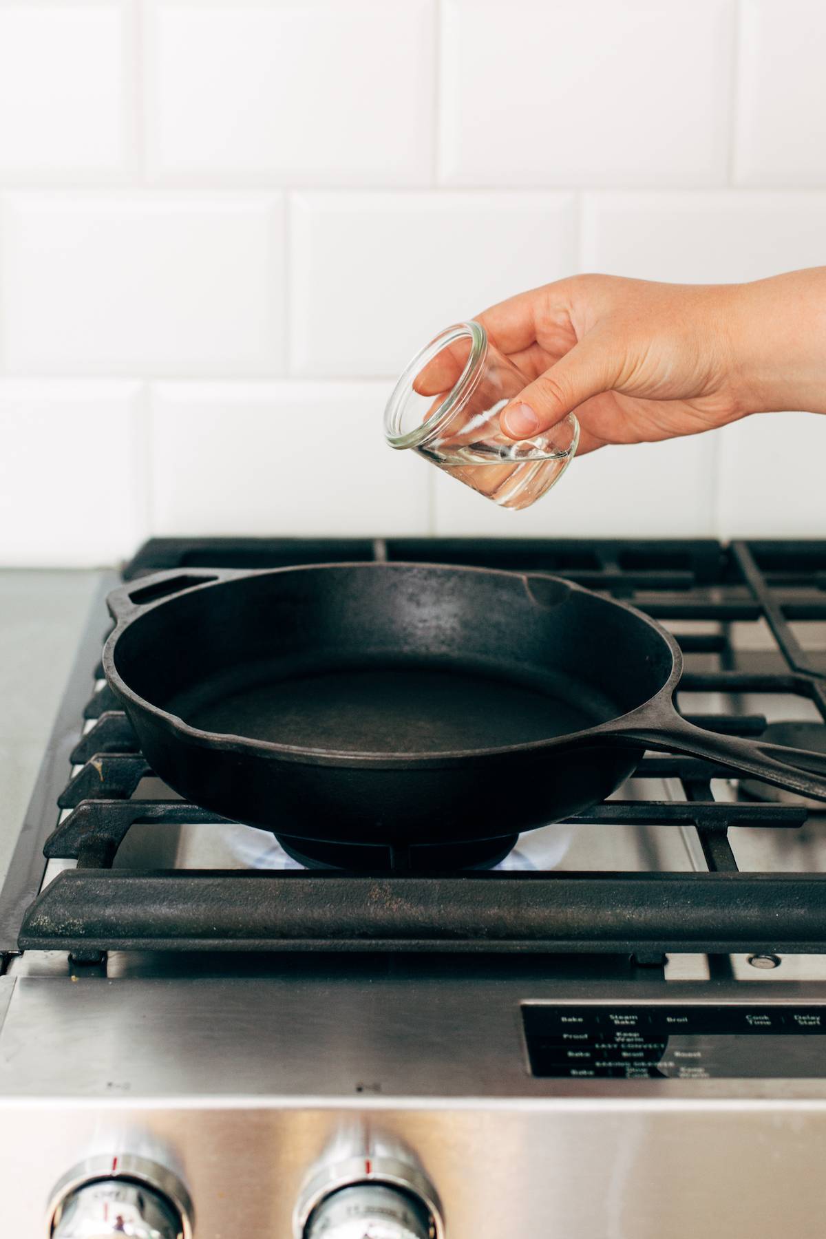 Person pouring oil into a cast iron skillet on the stove.