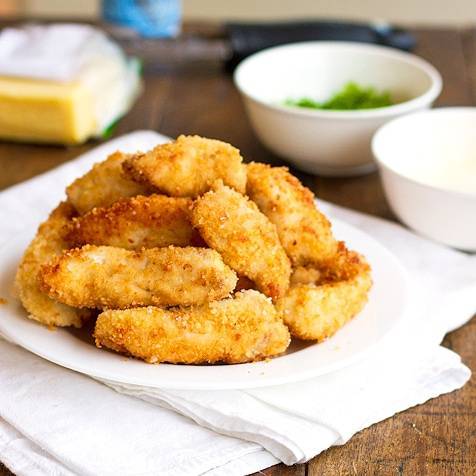 Parmesan chicken fingers stacked on a plate.