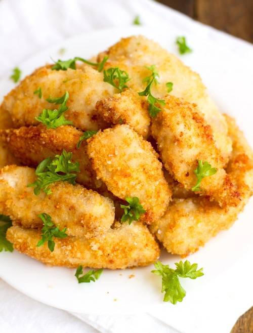 Parmesan chicken fingers stacked on a plate.