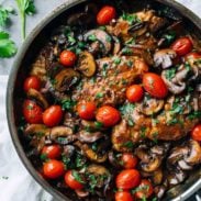 Chicken Marsala with tomatoes and mushrooms in a pan.