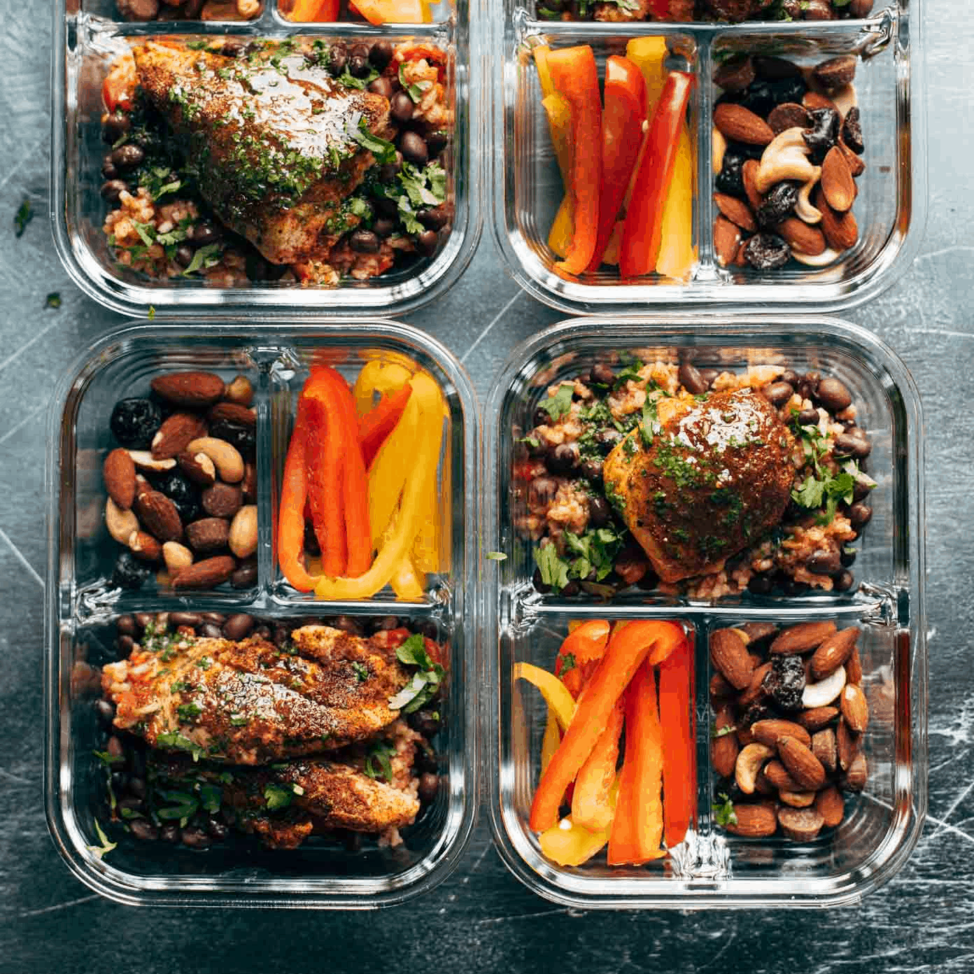Meal prep containers with chicken, nuts, and bell peppers.