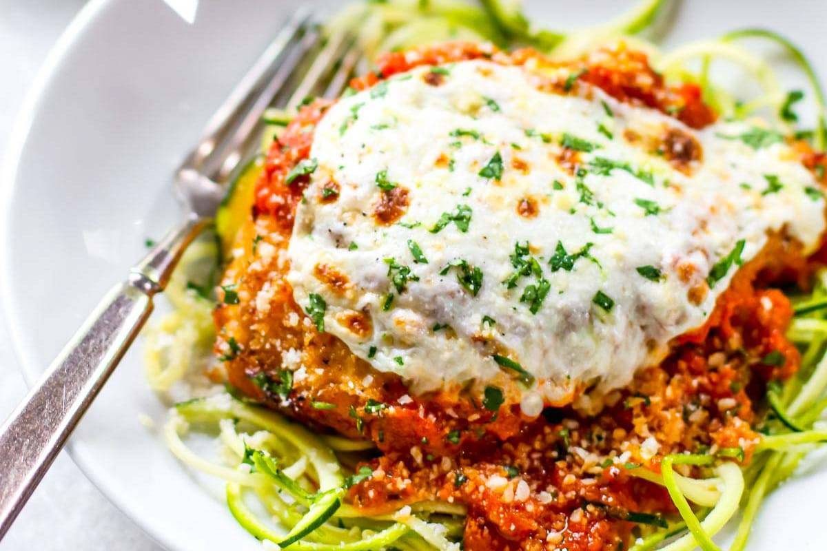 Healthy Chicken Parmesan on a white plate with a fork.
