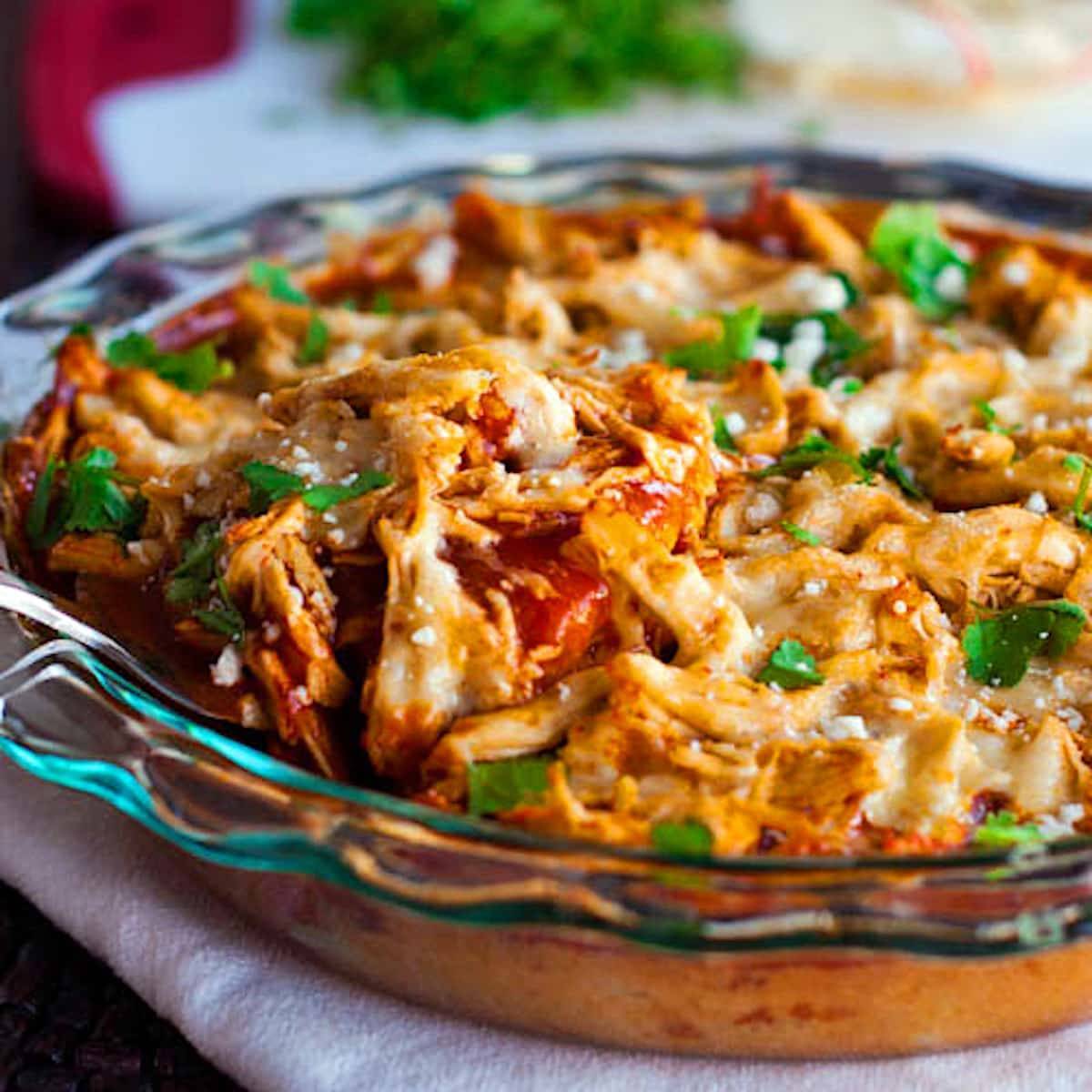 Chicken tamale pie topped with shredded chicken, enchilada sauce, and cheese in a clear dish.