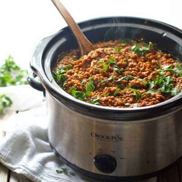 A crock pot full of red lentil curry with some green onions.