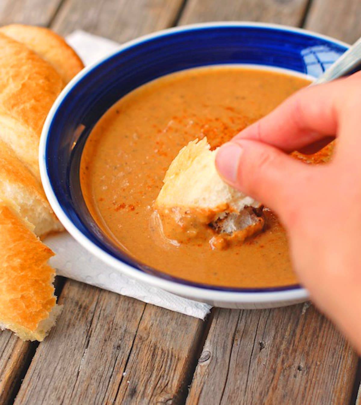 Pureed curry roasted red pepper and eggplant soup in a bowl with bread for dipping.