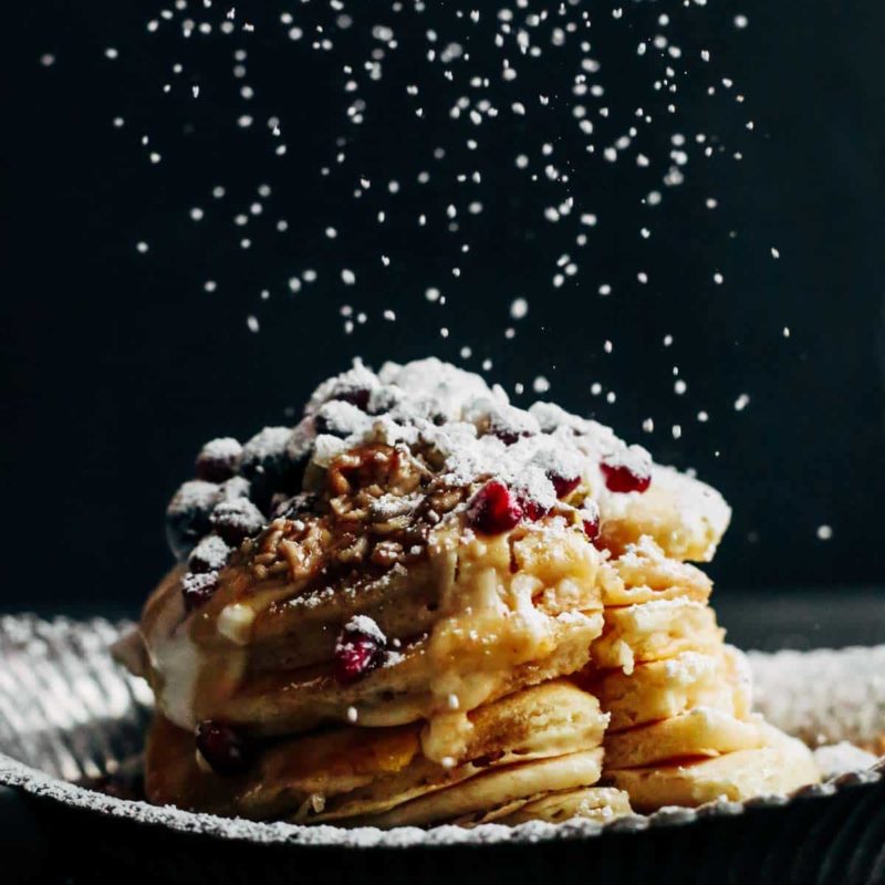 Powdered sugar being sprinkled on a stack of pancakes.