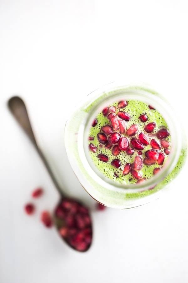 Green apple smoothie in a jar with pomegranate seeds.