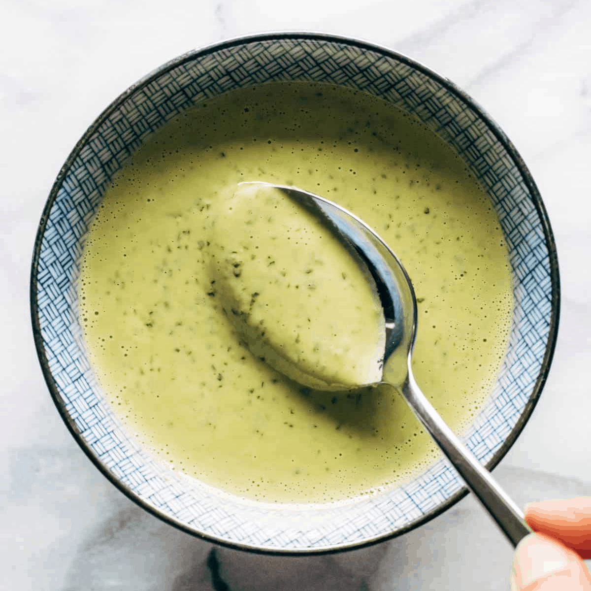 Green tahini sauce in a bowl with a spoon.