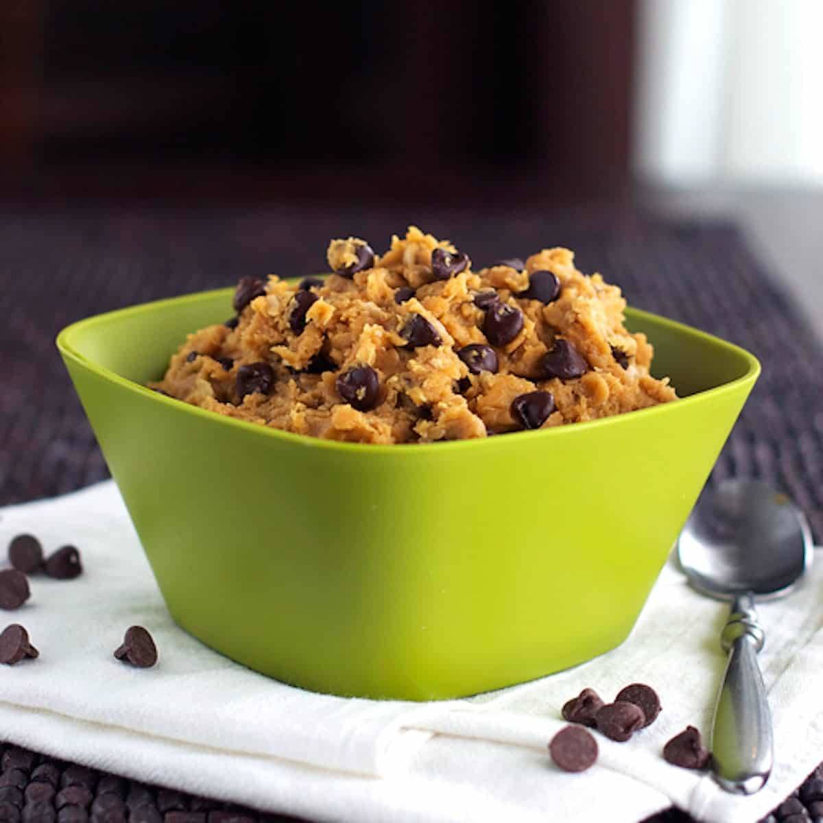 Chocolate chip peanut butter healthy cookie dough in a green bowl with a spoon.