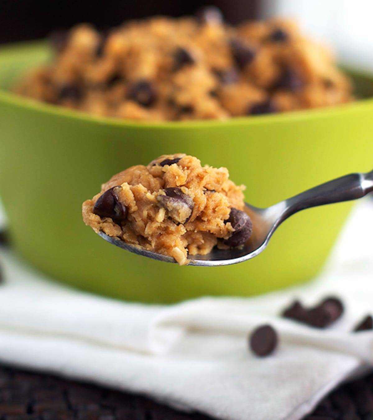 Chocolate chip peanut butter healthy cookie dough on a spoon in front of a green bowl.
