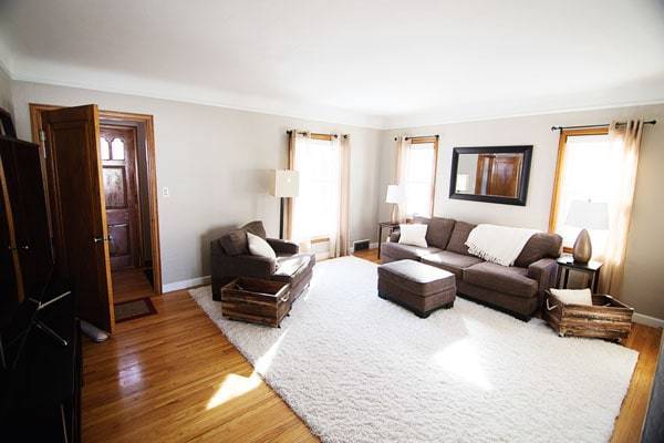 Ruangan yang bersih dengan set sofa coklat, karpet putih, dan lantai kayu.