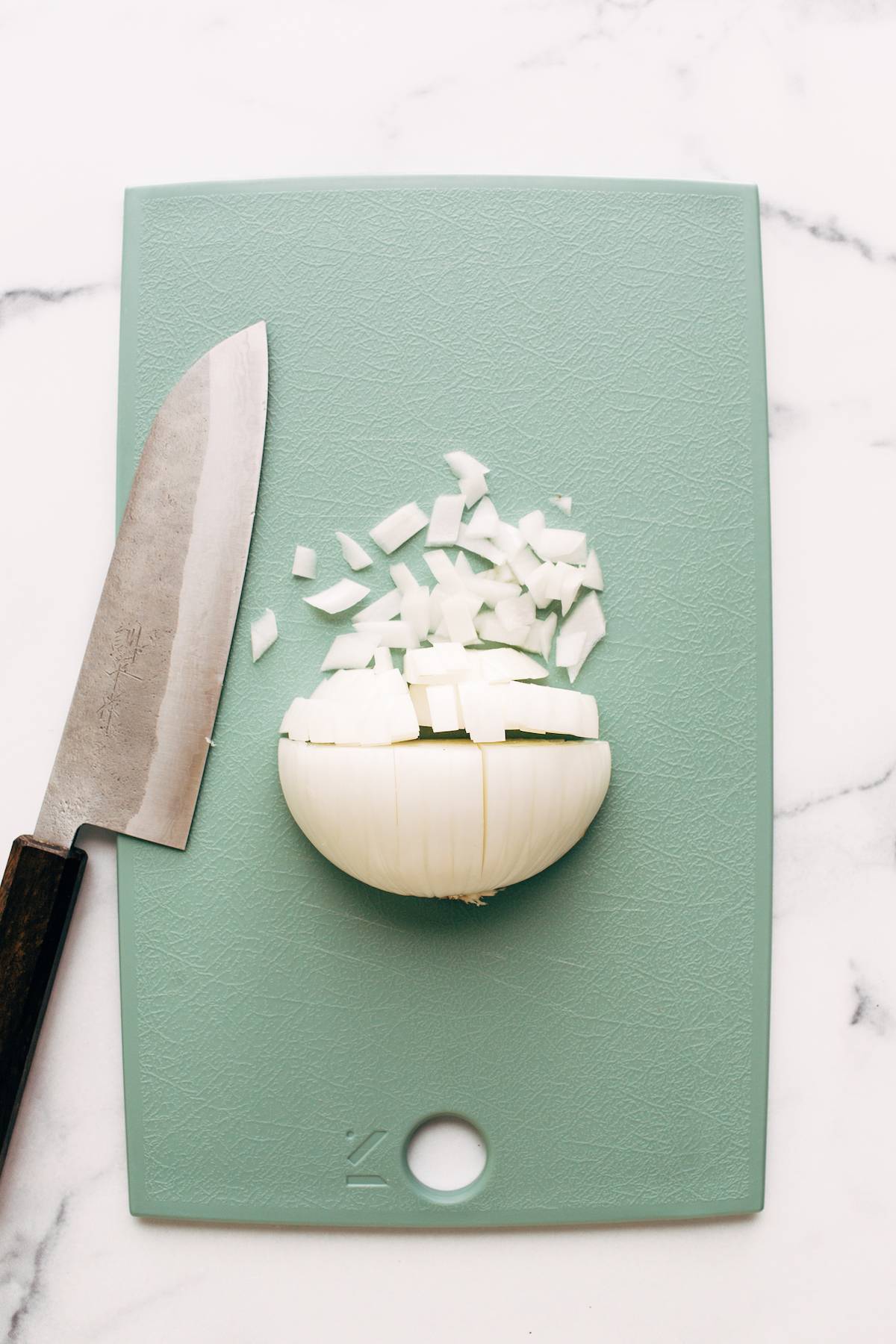 Half of an onion cut on a cutting board with a knife.