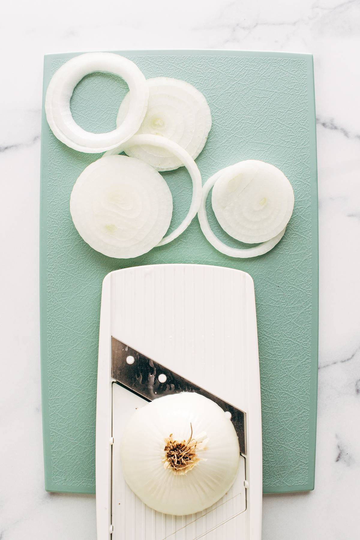 Rings of onions on a cutting board with a mandoline.