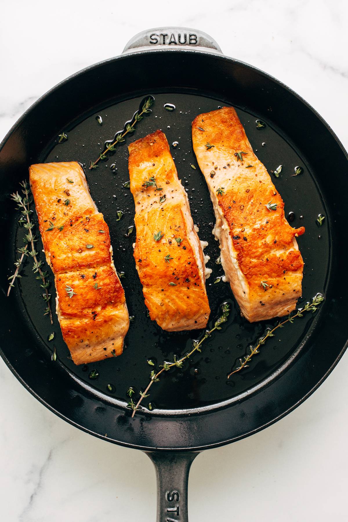 Three fillets of browned salmon in a cast iron pan.