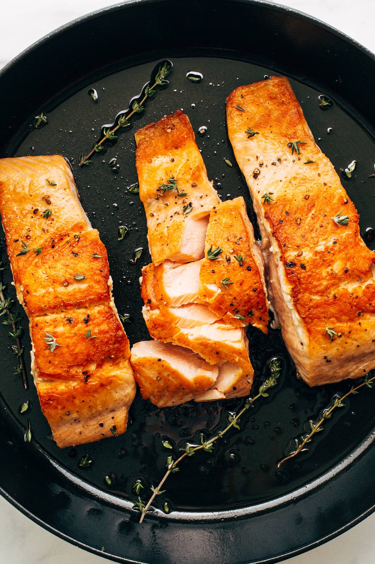 Three fillets of salmon in a skillet with the salmon flaked.