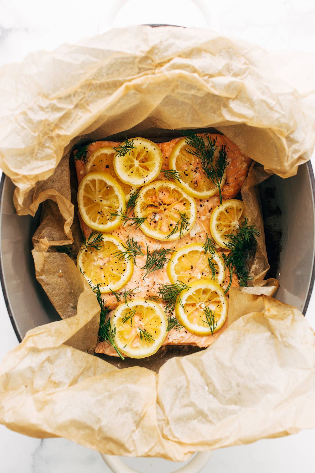 Four fillets of salmon in a dutch oven with lemon slices and dill.