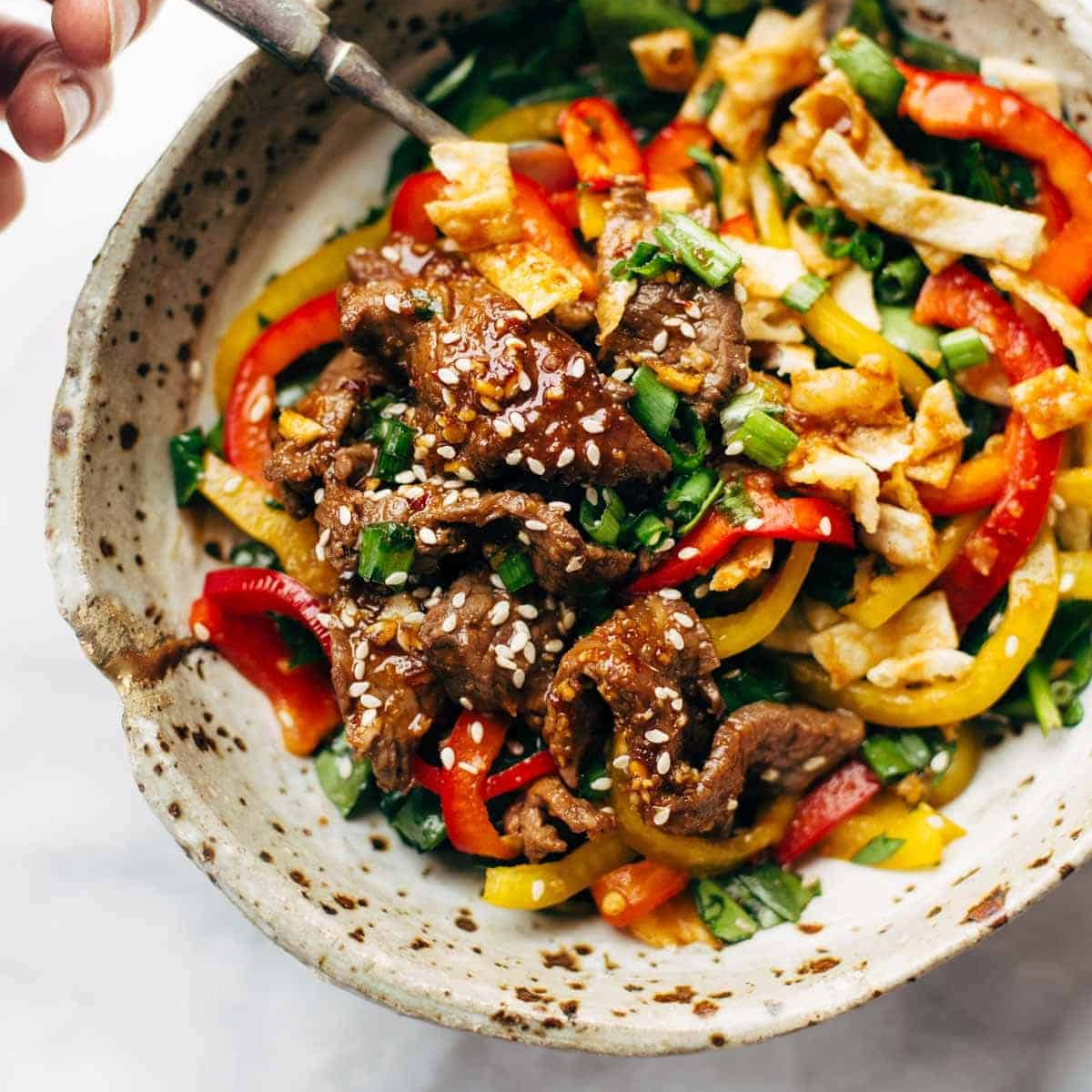 Korean steak sitting on a bed of colorful peppers.