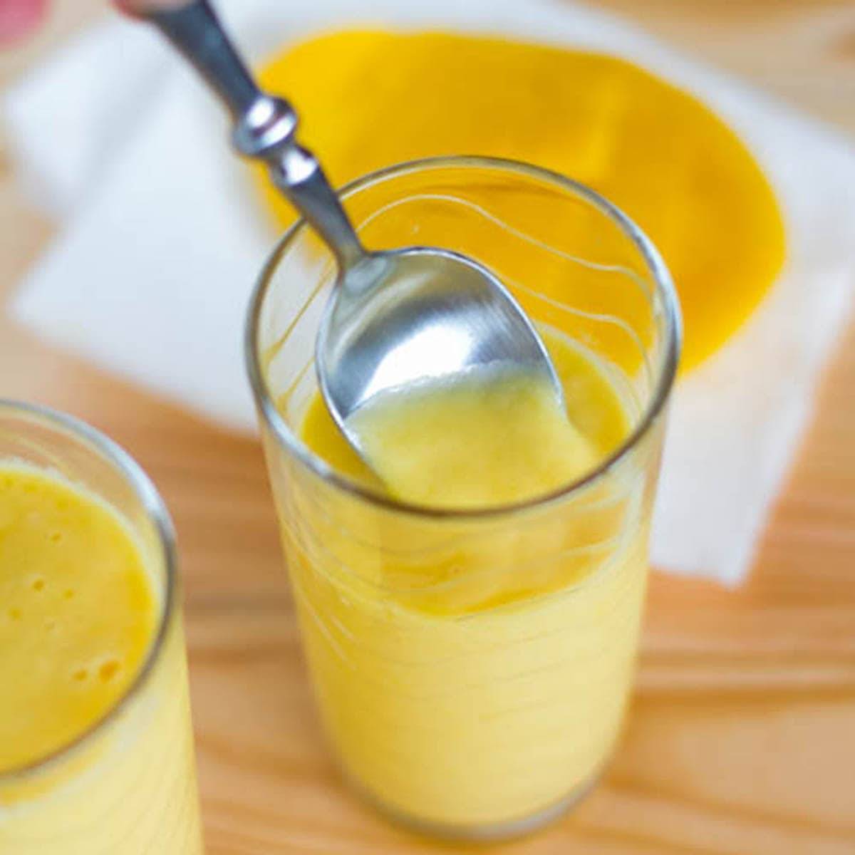 Mango lassi in a glass with a spoon.