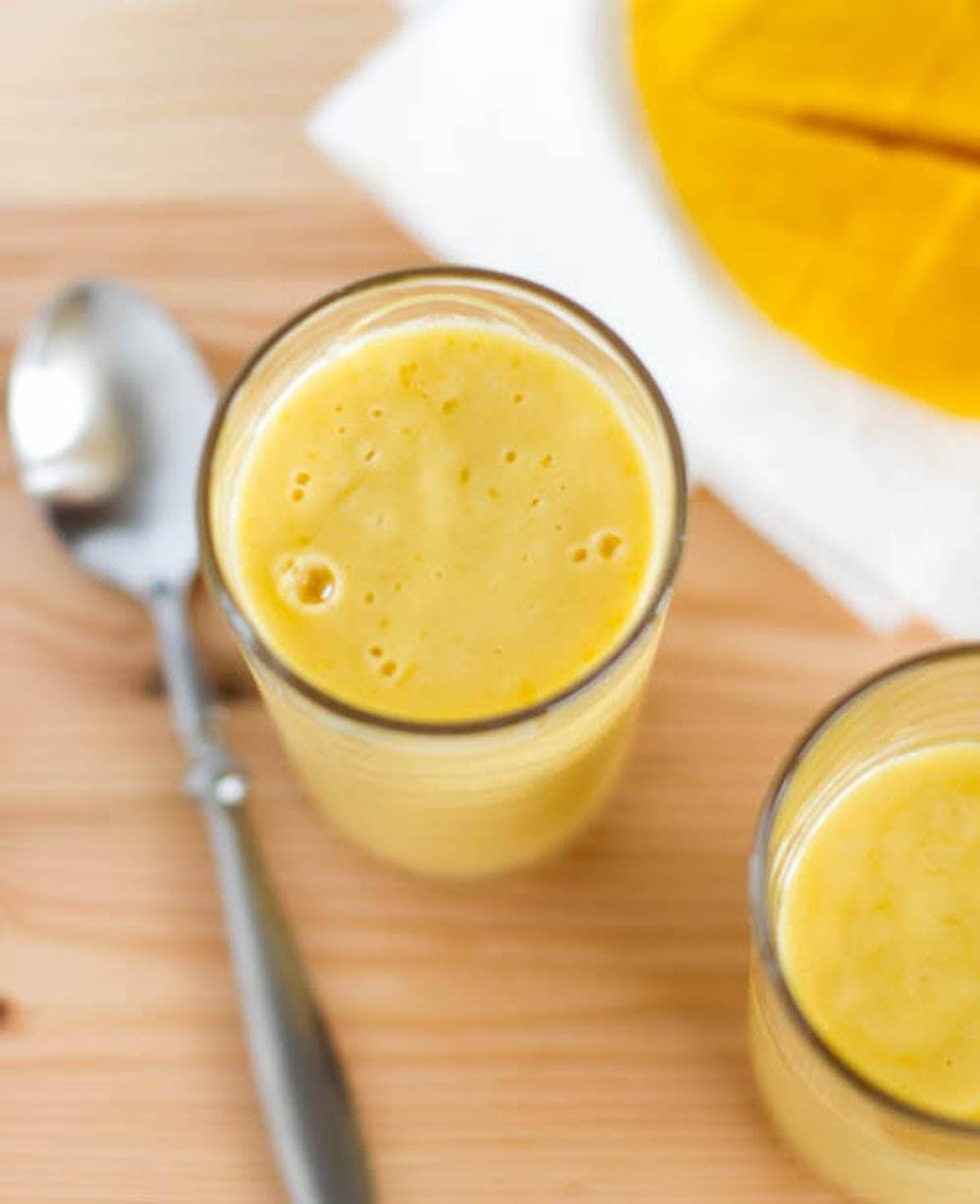 Mango lassi in two glasses with a spoon.