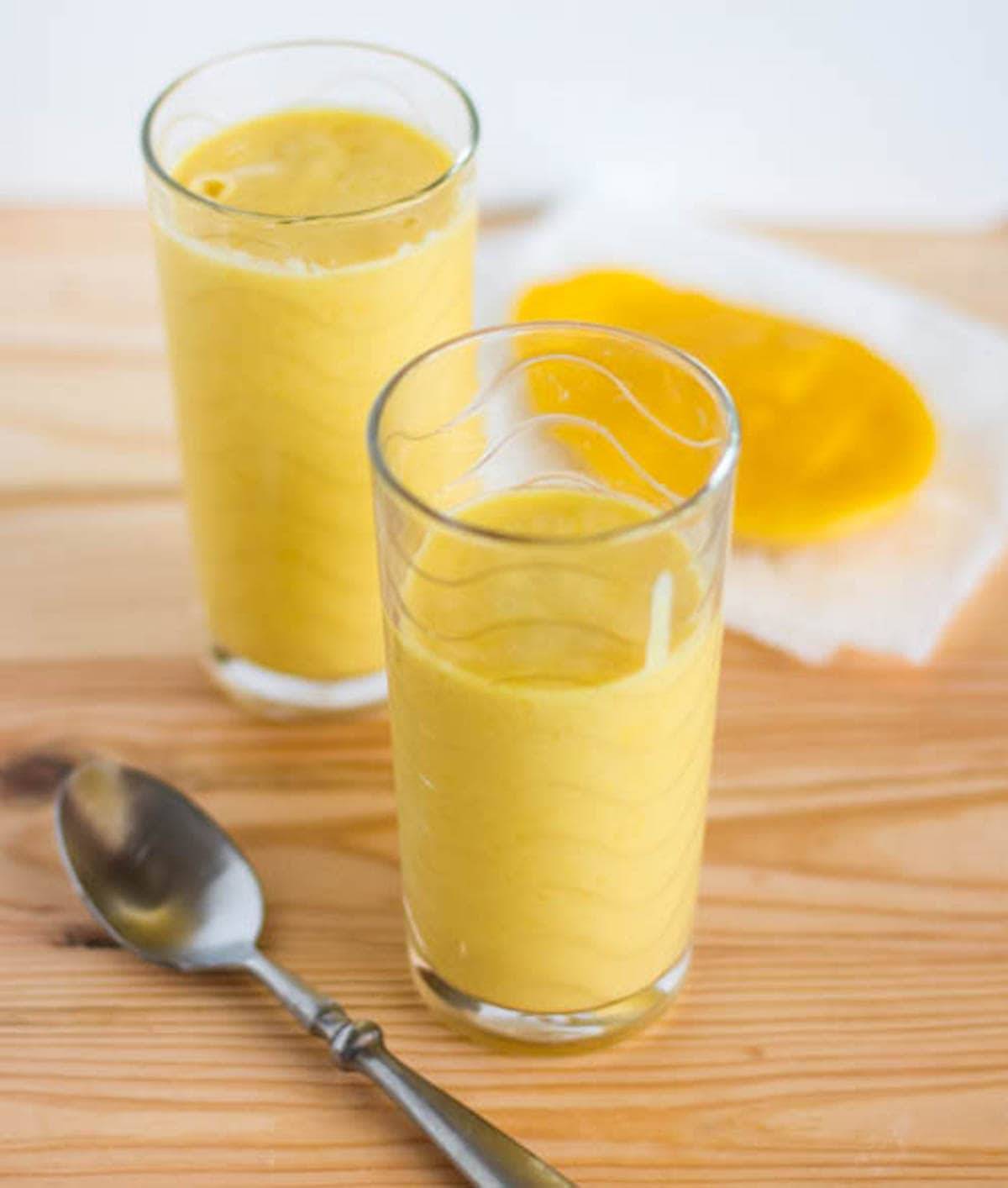 Mango lassi in two glasses with a spoon.