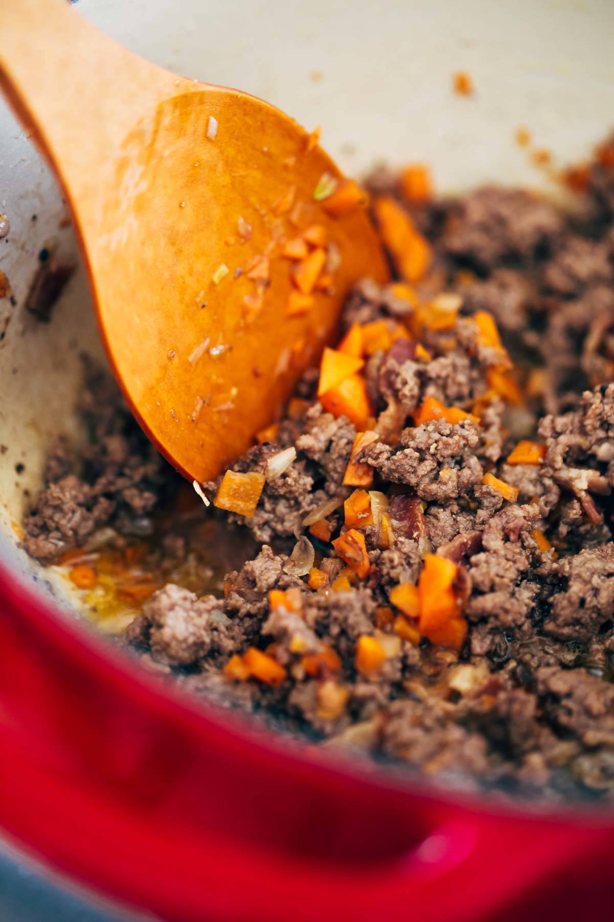Ground beef in a dutch oven with a wooden spoon.