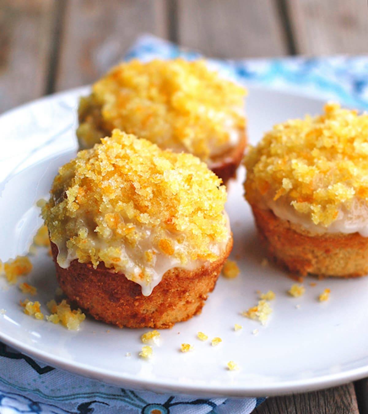 Whole wheat glazed orange muffins topped with a sugary zest on a white plate.