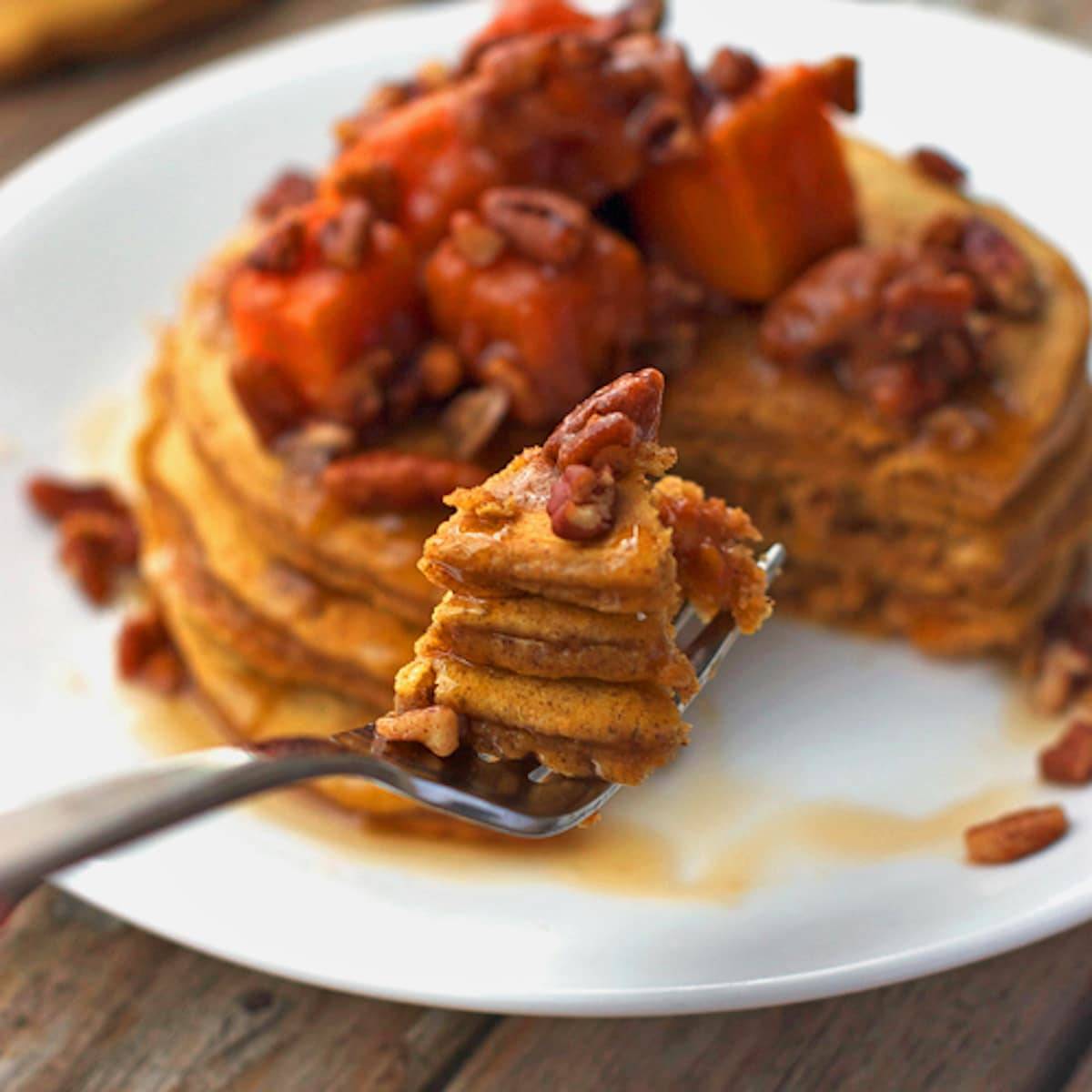 Butternut squash pecan pancakes topped with pecans and maple syrup on a plate and a fork.