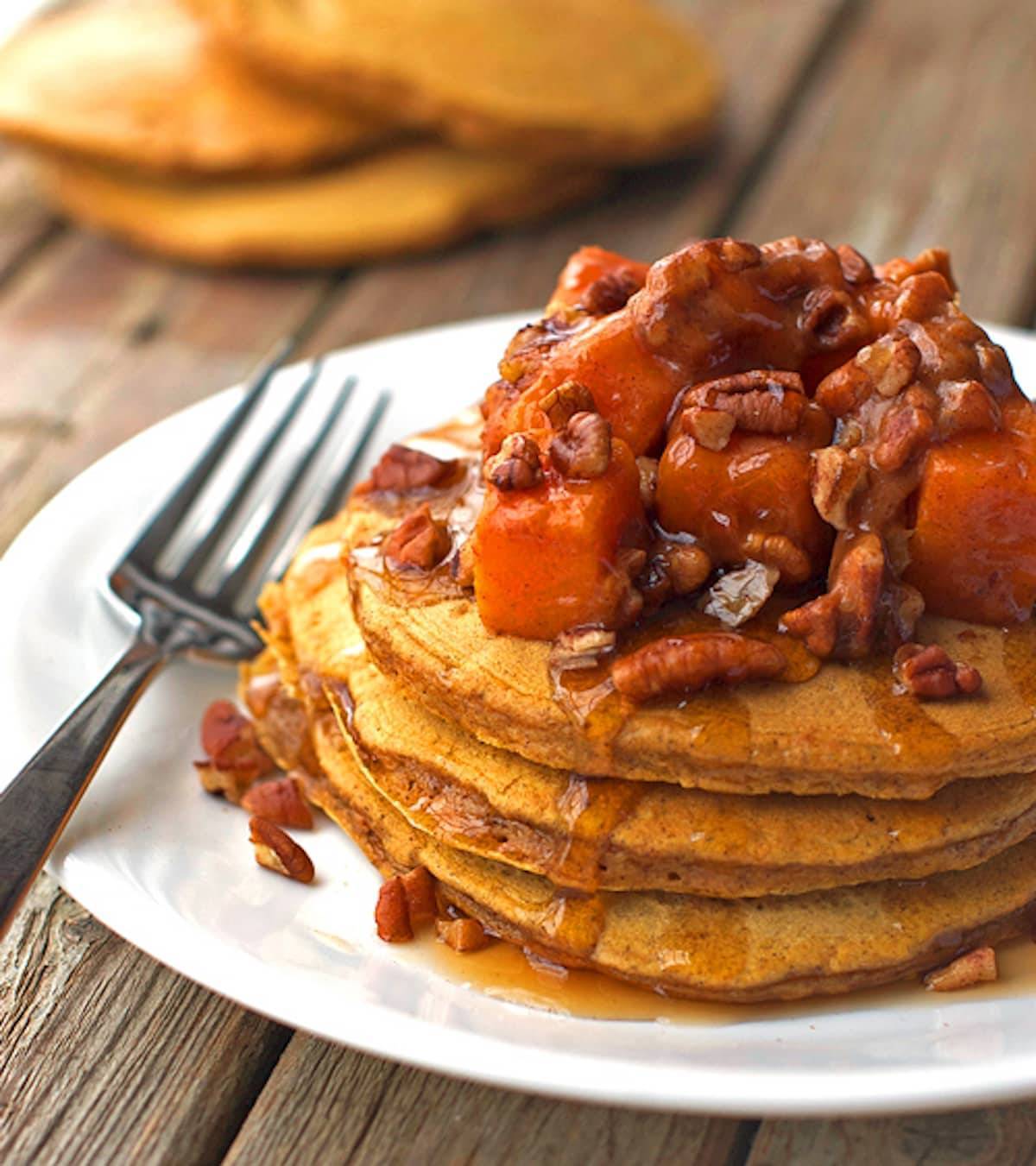 Butternut squash pecan pancakes topped with pecans and maple syrup on a white plate with a fork.