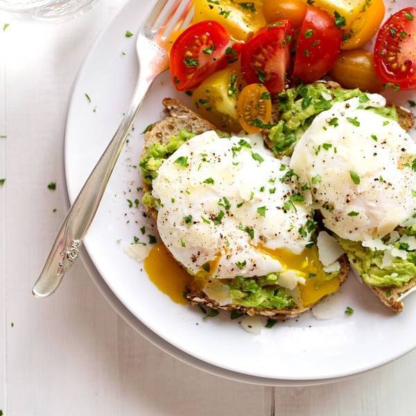 Oozy poached eggs on avocado toast with tomato on a plate